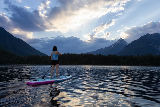 Une femme aventureuse fait du paddle dans un lac autour d'un paysage de montagnes canadiennes