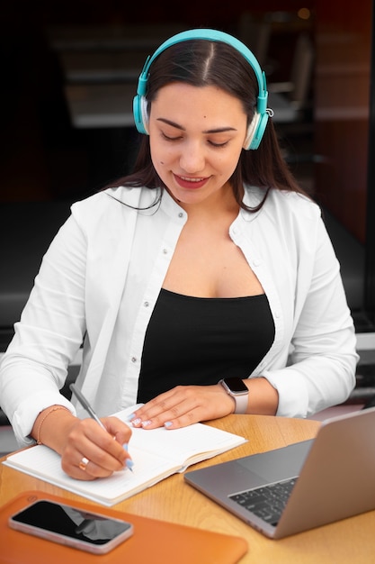 Photo femme ayant un appel vidéo sur un ordinateur portable dans un café et prenant des notes