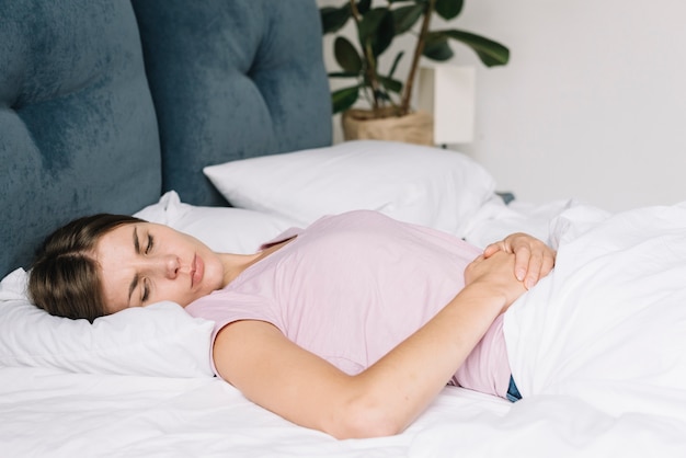 Femme ayant mal au ventre, couchée sur un lit