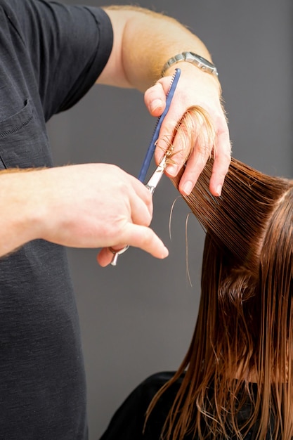 Femme ayant une nouvelle coupe de cheveux. Coiffeur masculin coupant les cheveux bruns avec des ciseaux dans un salon de coiffure.