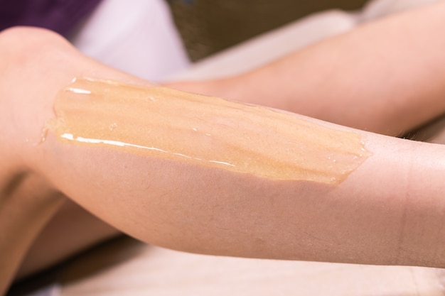Femme ayant une procédure d'épilation sur la jambe avec de la pâte à sucre dans le salon, gros plan. Cosmétologie
