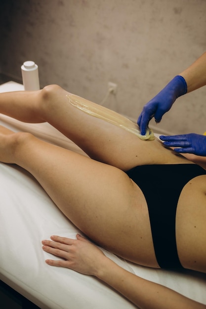 Femme ayant la procédure d'épilation sur la jambe avec de la pâte à sucre dans le salon