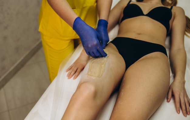 Femme ayant la procédure d'épilation sur la jambe avec de la pâte à sucre dans le salon