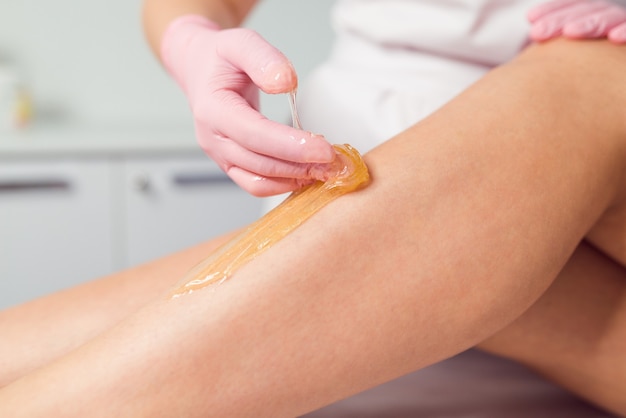 Femme ayant une procédure d'épilation sur les jambes avec de la pâte à sucre dans le salon