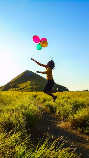 Photo une femme avec des ballons sautant sur la terre contre le ciel bleu