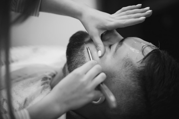 Femme Barber rase l'homme barbu au salon de coiffure