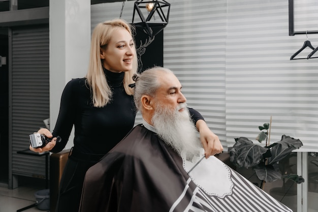 Femme barbier coupe les cheveux à un homme barbu âgé