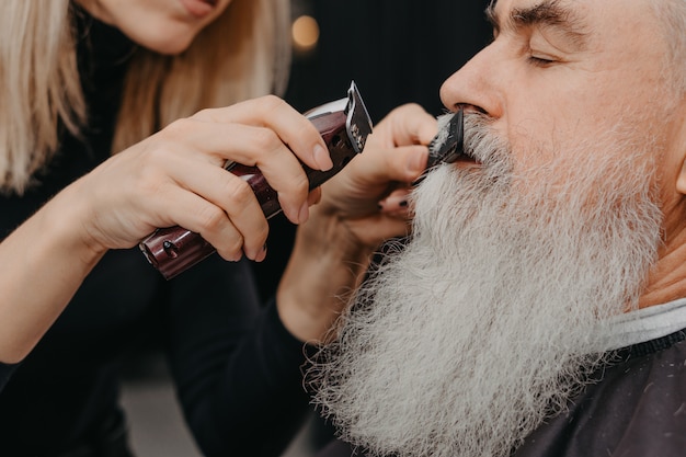 Femme barbier coupe moustache à un homme barbu âgé