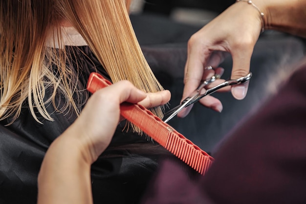 Une femme de barbier fait une jolie coiffure à la mode pour une jolie petite fille blonde dans un salon de coiffure moderne, un salon de coiffure. Le coiffeur fait la coiffure pour le jeune bébé dans le salon de coiffure. Concept coiffure et beauté