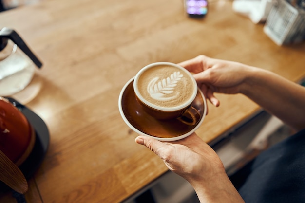 Femme barista donnant l'ordre au client au café branché. Tasse à café avec art latte.