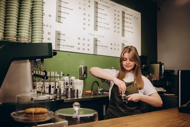 Femme barista souriante debout avec un porte-café plein de café moulu dans ses mains routine de travail bariste