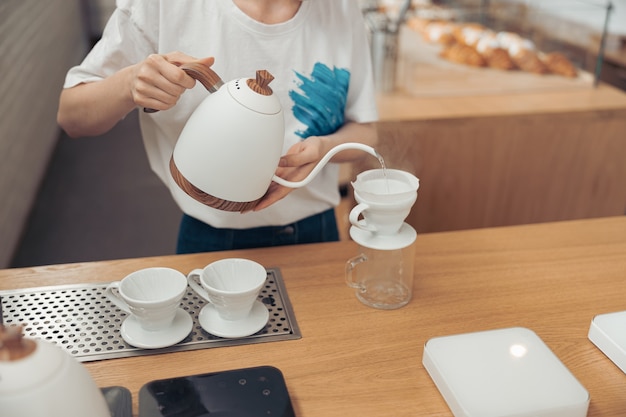 Femme barista verser de l'eau bouillie à travers un filtre dans une tasse en verre