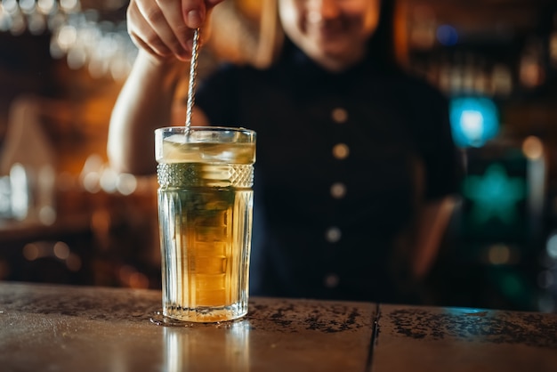 Femme barman remuer la boisson dans un verre