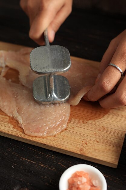 Femme bat le filet de poulet à la main avec du marteau à viande