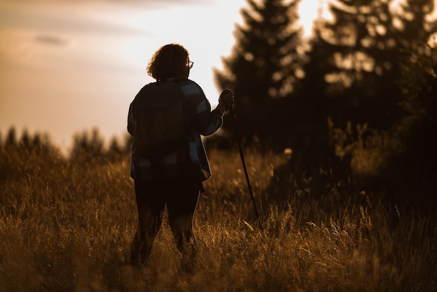 Une femme avec des bâtons un sac à dos sur le dos et un équipement d'alpinisme marchant au sommet d'une montagne au coucher du soleil