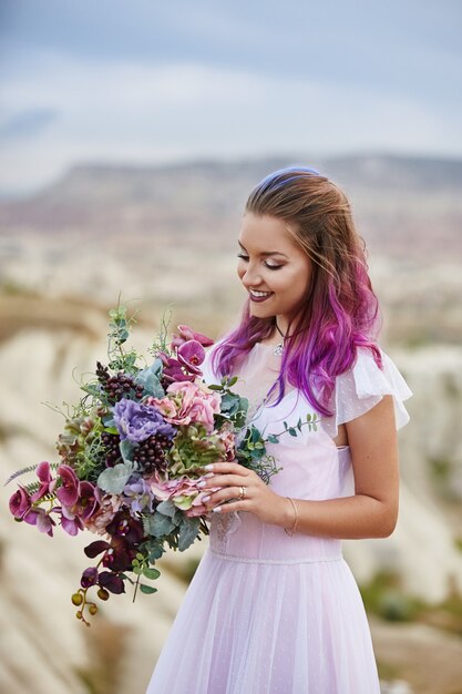 Femme avec un beau bouquet de fleurs dans ses mains se dresse sur la montagne dans les rayons du soleil de l'aube