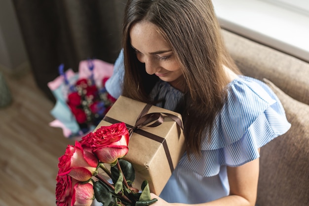 Femme avec un beau bouquet de roses fraîches et une boîte-cadeau dans ses mains à la maison