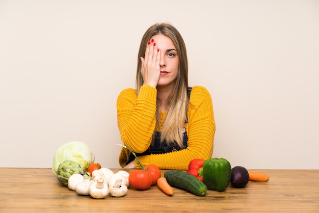 Femme avec beaucoup de légumes couvrant un oeil à la main