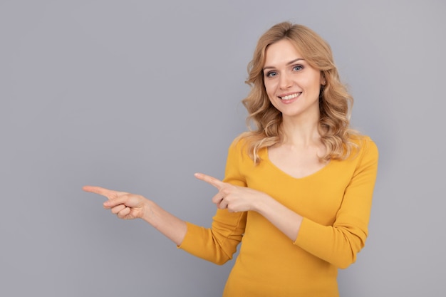 Femme de beauté blonde joyeuse aux cheveux bouclés pointant le doigt sur l'espace de copie, publicité.