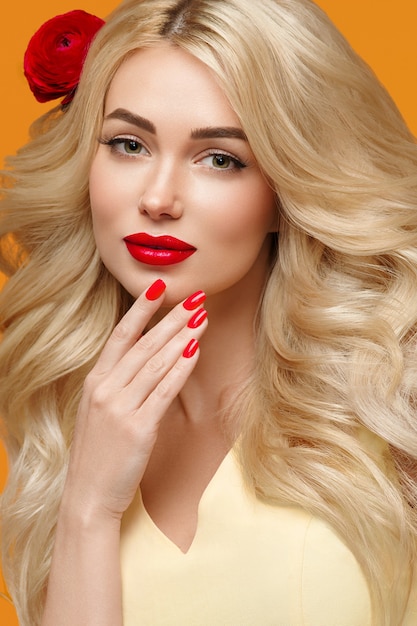 Femme de beauté avec de longs cheveux blonds bouclés cheveux de fleur ongles manucurés couleurs à la mode orange et jaune