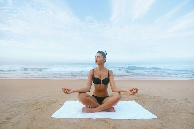 Une femme de beauté pratique le yoga et médite en position du lotus sur la plage. Méditation. Mode de vie actif. Concept sain et yoga. Remise en forme et sport