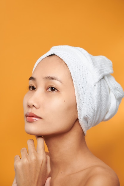 Femme de beauté de soins de la peau de station thermale utilisant la serviette de cheveux après le traitement de beauté. Belle jeune femme avec une peau parfaite isolée sur fond orange.