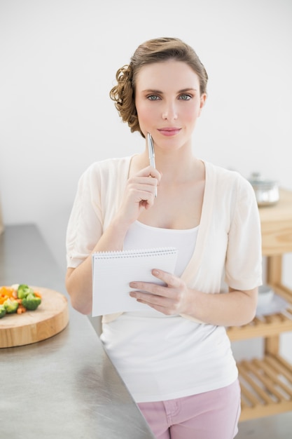 Femme belle pensée, écrire une liste de courses debout dans la cuisine