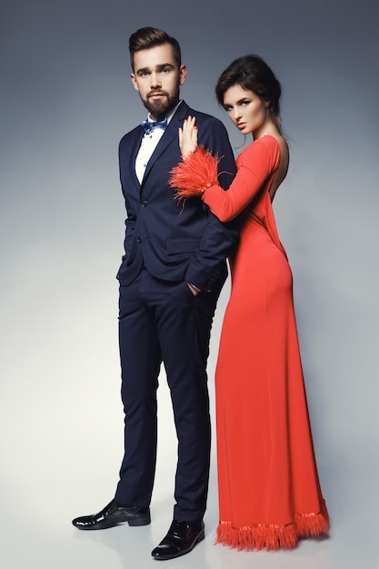 Femme en belle robe rouge et homme portant un costume classique bleu avec noeud papillon.