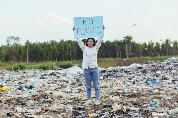 Une femme bénévole piquetage dans une décharge avec une affiche sans plastique, une militante lutte contre la pollution de l'environnement