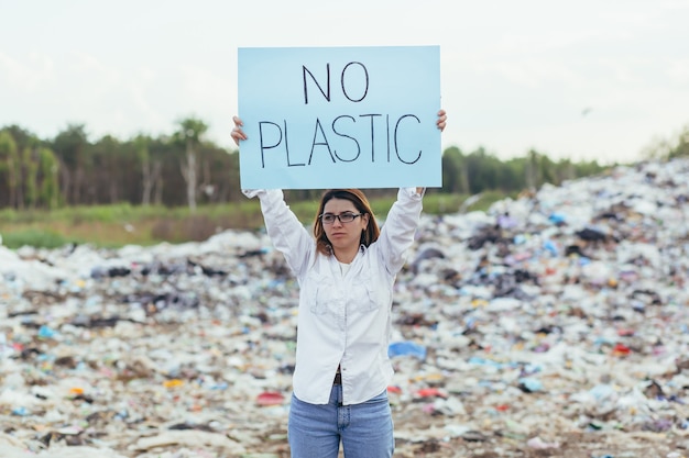 Une femme bénévole piquetage dans une décharge avec une affiche sans plastique, une militante lutte contre la pollution de l'environnement