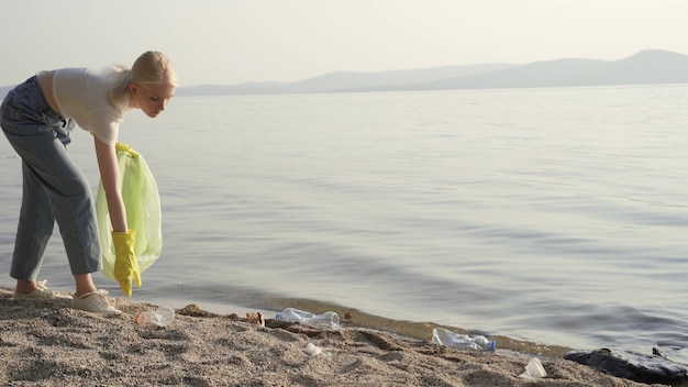 Une femme bénévole portant des gants en caoutchouc et un sac en plastique à la main ramasse des ordures sur la rive du lac. Purification des réservoirs et de l'environnement. 4K UHD