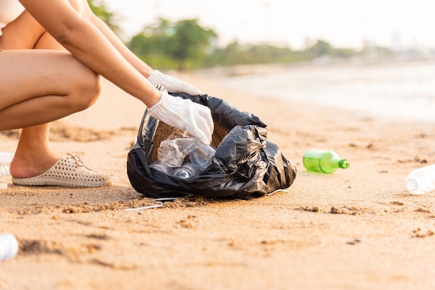 Femme bénévole ramassant une bouteille en plastique dans un sac en plastique noir pour nettoyer la plage