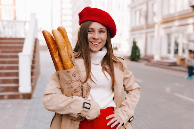 Femme en béret rouge avec sac de baguettes marchant à la maison avec un sourire heureux