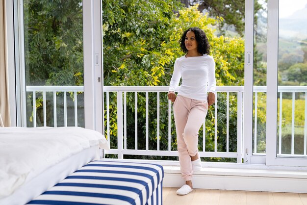 Photo une femme bi-raciale heureuse en pantoufles se détendant sur le balcon de sa chambre avec des cimes d'arbres en arrière-plan. bien-être, vie domestique et style de vie, inchangés.