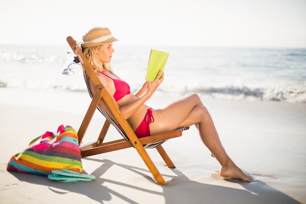 Femme en bikini assise sur un fauteuil et livre de lecture