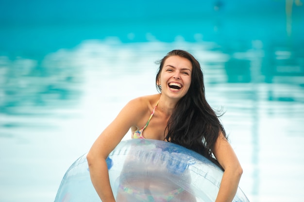 Une femme en bikini avec un cercle gonflable en caoutchouc jouant et s'amusant dans la piscine du parc d'attractions en été