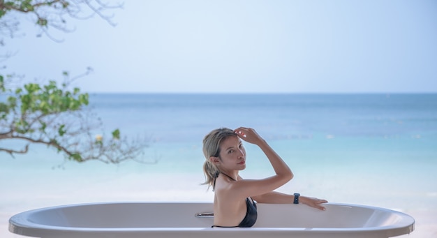 Femme en bikini noir se détendre dans la baignoire avec fond océan plage.