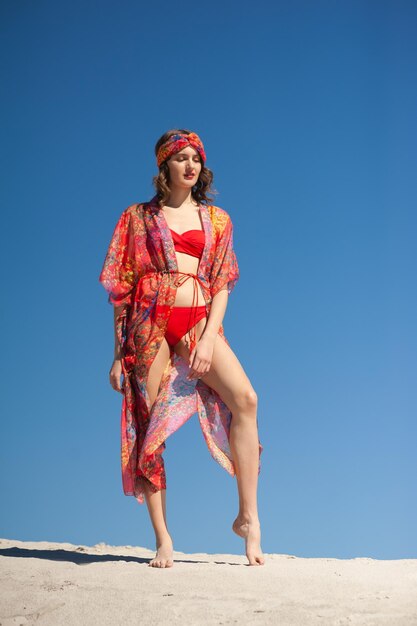 Une femme en bikini rouge se tient sur un rebord avec un ciel bleu derrière elle.