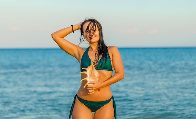 Une femme en bikini vert avec une coquille sur la tête se tient sur la plage.