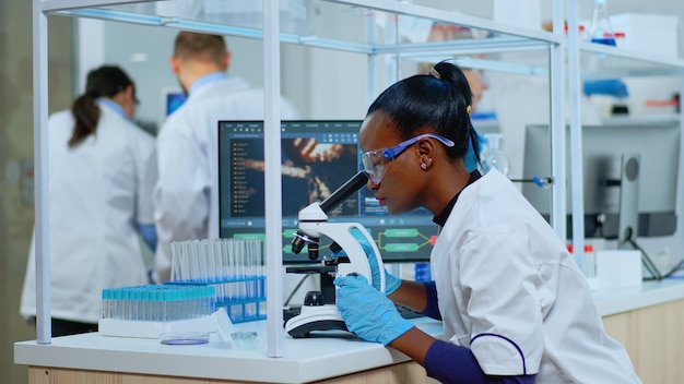 Femme biochimiste noire assise dans un laboratoire équipé moderne analysant des tests sanguins. Équipe multiethnique examinant l'évolution du virus à l'aide de la haute technologie pour la recherche scientifique sur le développement de traitements contre covid19