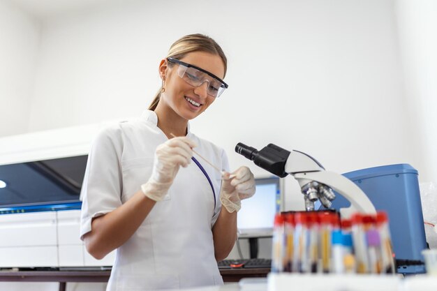 Femme biologiste utilisant une micro pipette avec tube à essai et bécher pour une expérience en laboratoire scientifique Spécialiste en biochimie travaillant avec du matériel de laboratoire et de la verrerie pour le développement