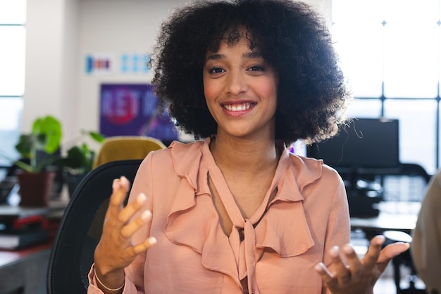 Une femme biraciale heureuse parle en regardant la caméra pendant un appel vidéo au bureau.