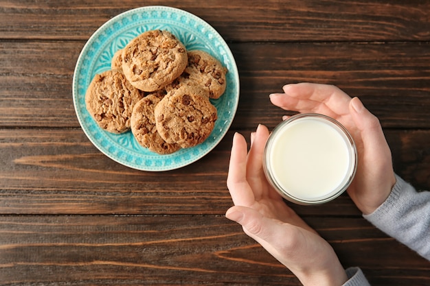 Femme avec des biscuits à l'avoine et un verre de lait à table en bois