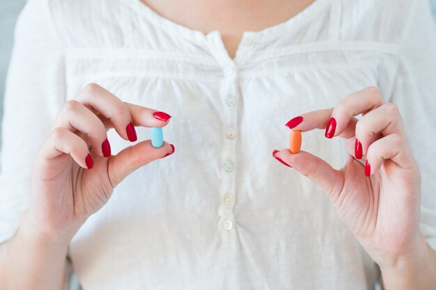 Femme en blanc tenant des pilules rouges et bleues. traitement médicamenteux et santé