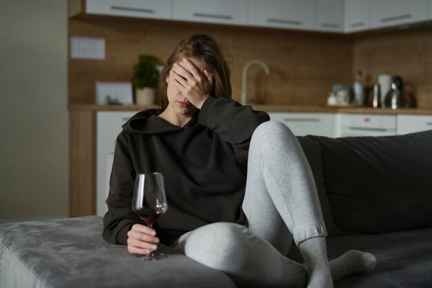 Photo une femme blanche alcoolique assise sur le canapé et tenant un verre de vin.