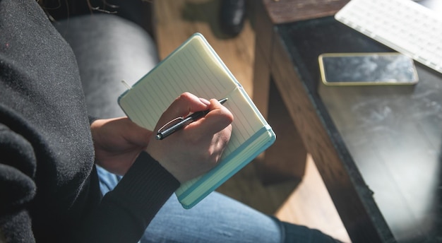 Une femme blanche écrit dans un bloc-notes.