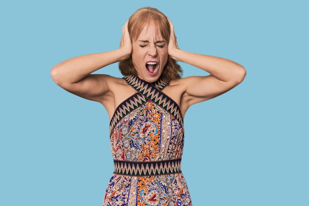 Une femme blanche rousse d'âge moyen dans un studio couvrant les oreilles avec ses mains en essayant de ne pas entendre un bruit trop fort