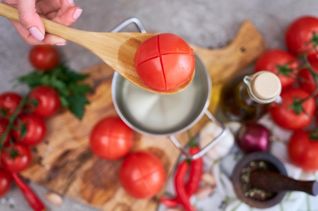 Femme blanchissant une tomate tenant au-dessus d'une casserole avec de l'eau chaude pour l'éplucher davantage