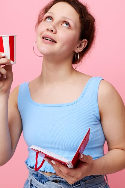 Femme avec bloc-notes et verre dans les mains boit fond rose inchangé