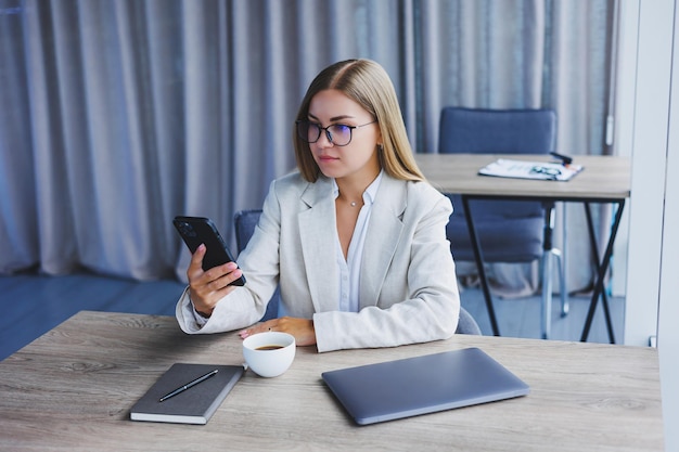 Femme blogueuse avec téléphone mobile numérique souriant pendant la pause-café à l'intérieur du café femme européenne heureuse avec smartphone et boisson à la caféine posant